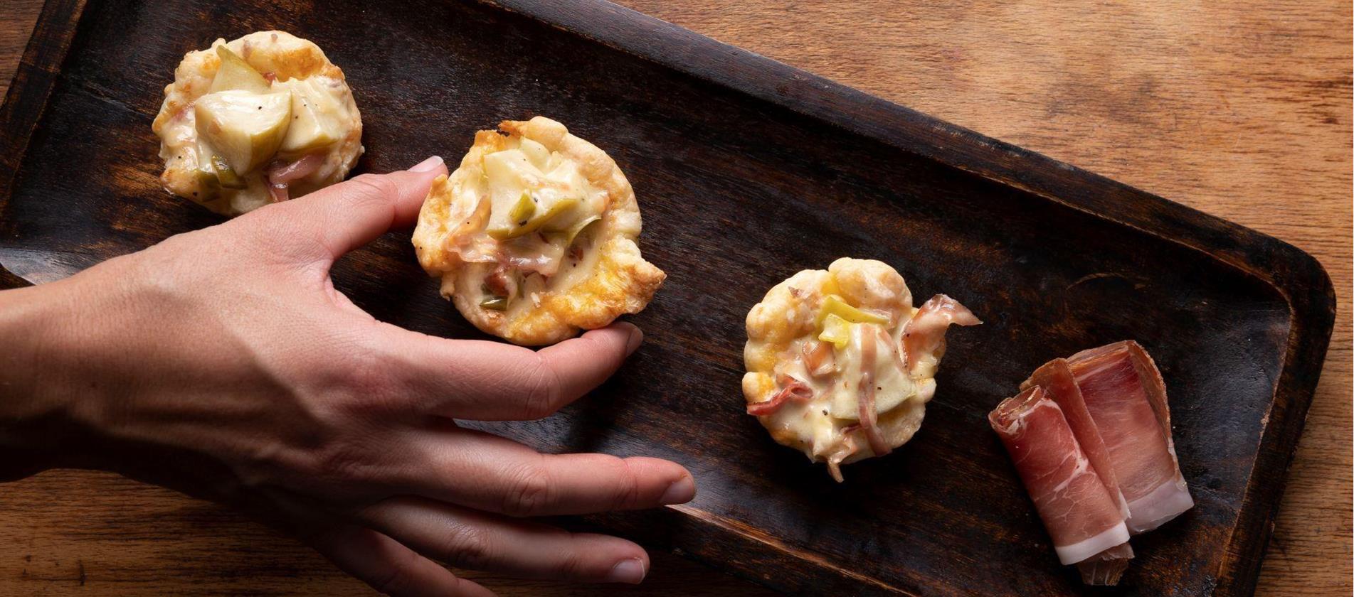 Barchette di pasta sfoglia con mele e speck servite su una teglia scura.