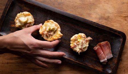 Barchette di pasta sfoglia con mele e speck servite su una teglia scura.