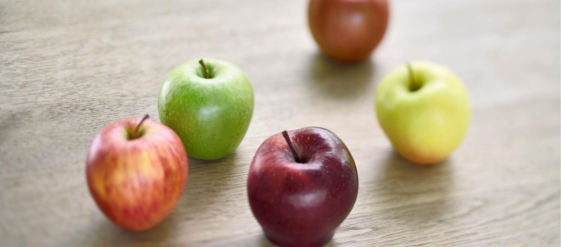 Diverse mele dell’Alto Adige di colori differenti appoggiate su un tavolo in legno.