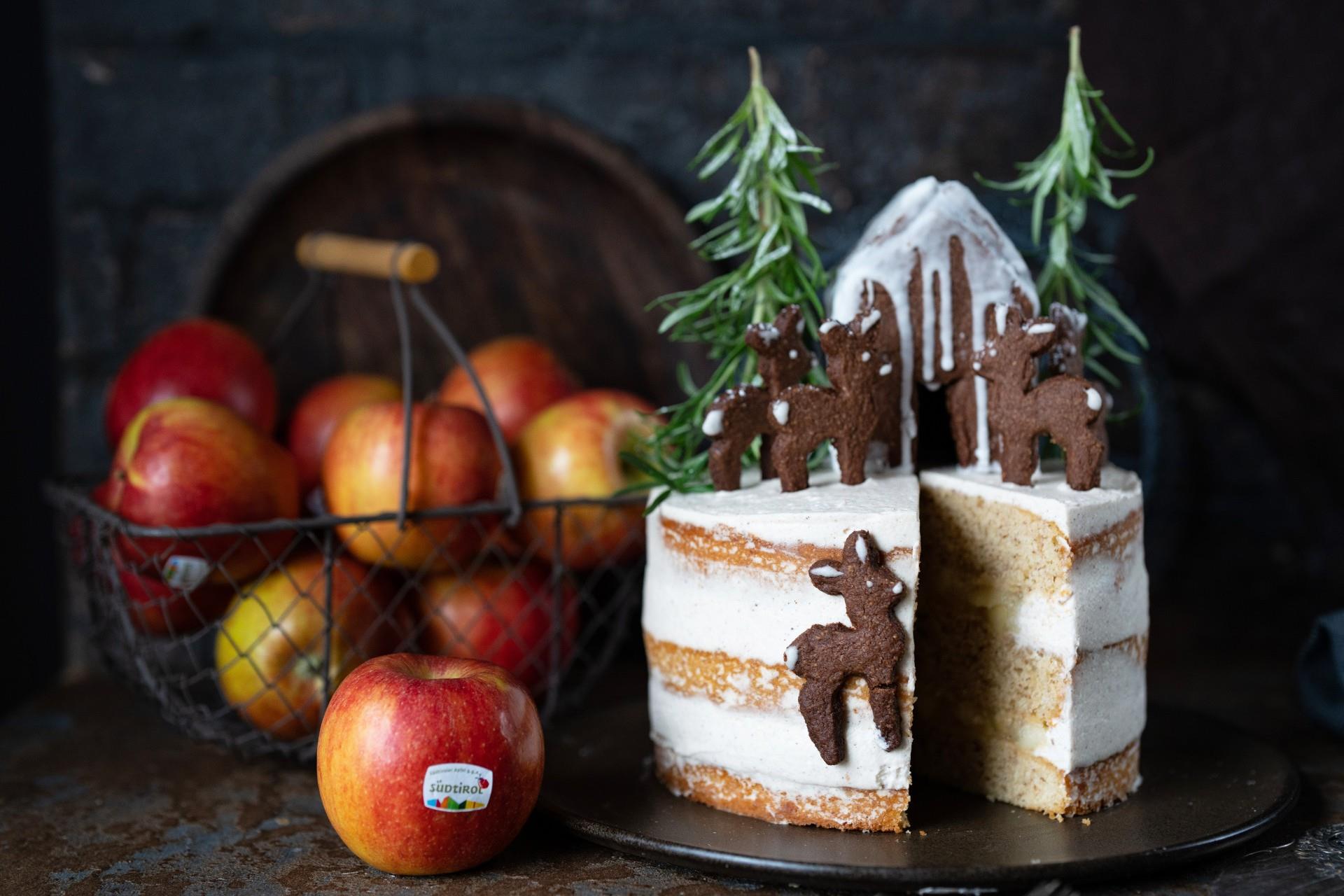 Torta alle mele decorata in stile invernale con mele e piccoli abeti su un tavolo rustico.