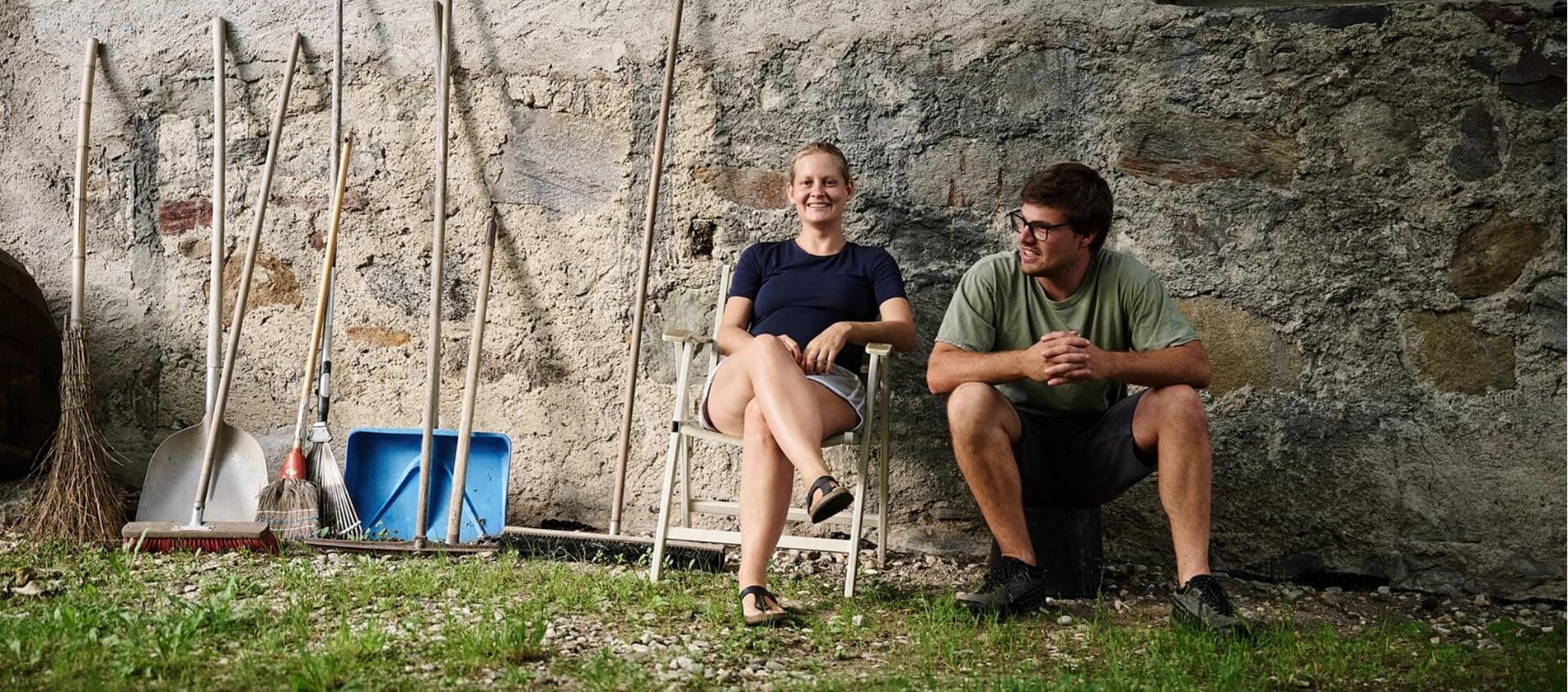 Andrea Erlacher e Jacob Gamper siedono insieme davanti al maso, accanto a diversi attrezzi da lavoro.