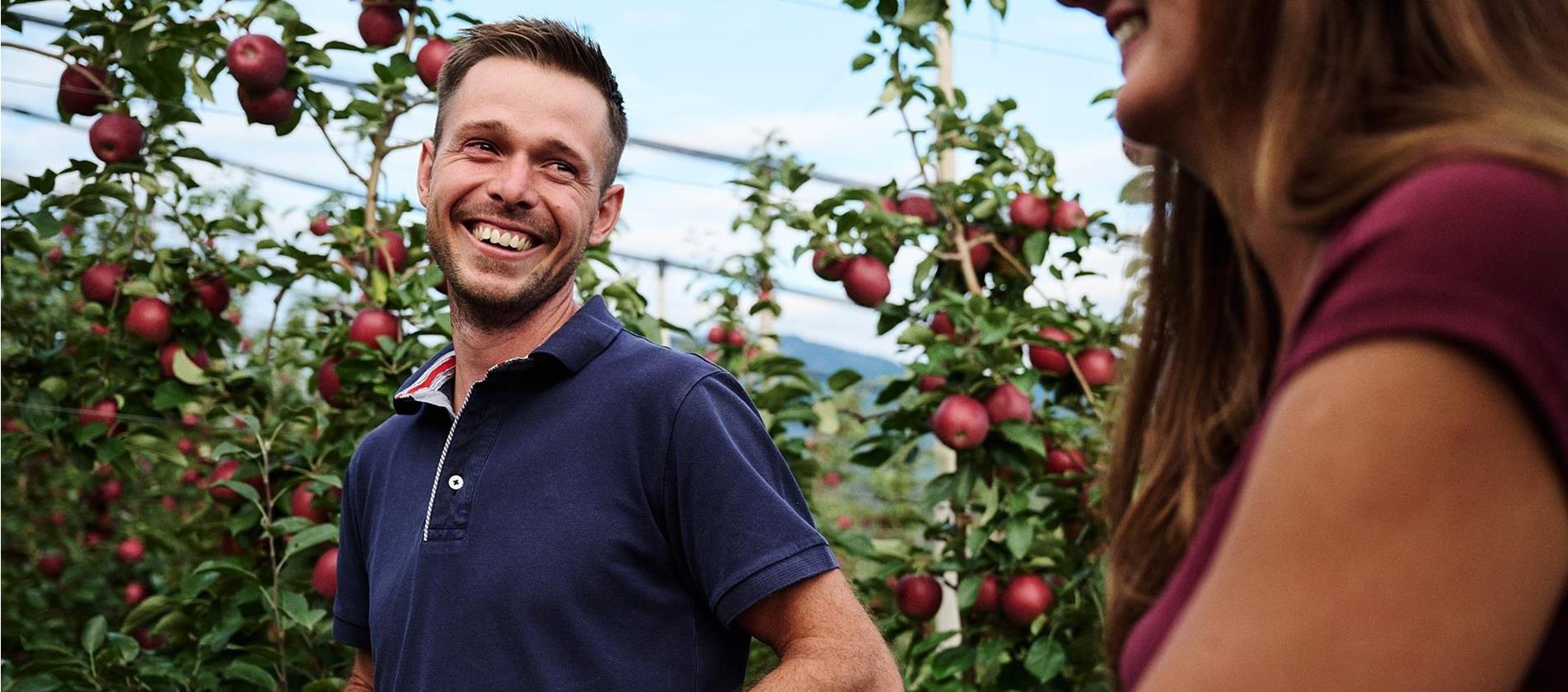 Due persone si sorridono in un meleto con mele mature