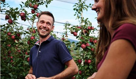 Due persone si sorridono in un meleto con mele mature
