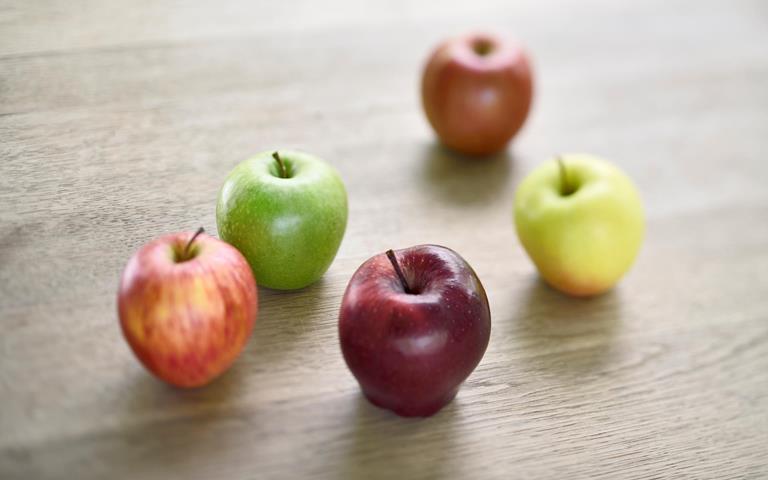 Mele dell’Alto Adige di diversi colori disposte su un tavolo in legno.